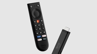 Vor grauem Hintergrund sind ein Amazon Fire TV Stick und die dazugehörige Fernbedienung freigestellt dargestellt. Die schwarze Fernbedienung zeigt ein Steuerkreuz, Lautstärketasten, mehrere Funktionstasten sowie Schnellzugriffe für Prime Video, Netflix, YouTube und Disney+. Daneben ist der schwarze Fire TV Stick mit HDMI-Anschluss und dem Aufdruck „fire tv“ zu sehen. Beide Geräte sind leicht schräg ausgerichtet und scheinen vor dem Hintergrund zu schweben.