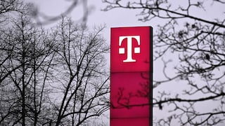 Hohe, pinkfarbene Stele mit weißem Telekom-Logo vor einem grauen Himmel. Rund um die Stele sind zahlreiche kahle Baumäste zu sehen, einige davon unscharf im Vordergrund.