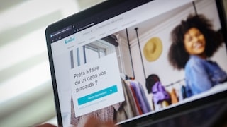 Laptop mit geöffneter Vinted-Webseite. Auf der französischsprachigen Startseite sind das Vinted-Logo, ein Kleiderschrank mit Kleidung sowie eine Person im Hintergrund zu sehen. Im Vordergrund befindet sich ein Feld mit dem Text "Prêts à faire du tri dans vos placards ?" und einer türkisfarbenen Schaltfläche.