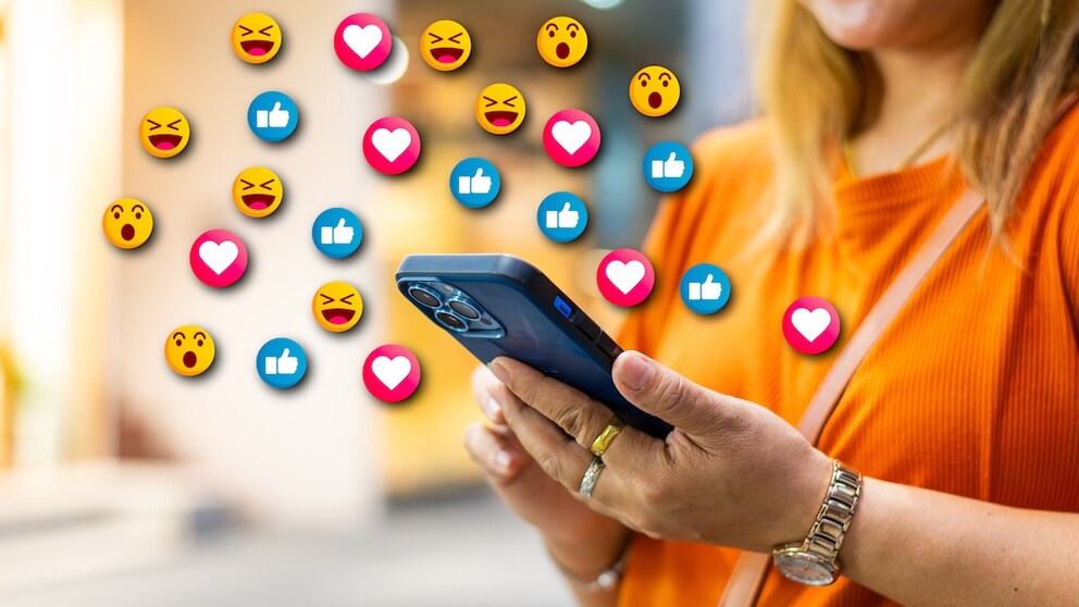 Frau nutzt ihr Smartphone, über dem symbolisch verschiedene Emojis erscheinen