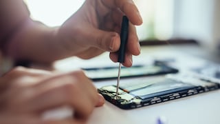 Hände reparieren mit einem Schraubendreher das geöffnete Innere eines Smartphones auf einem Tisch
