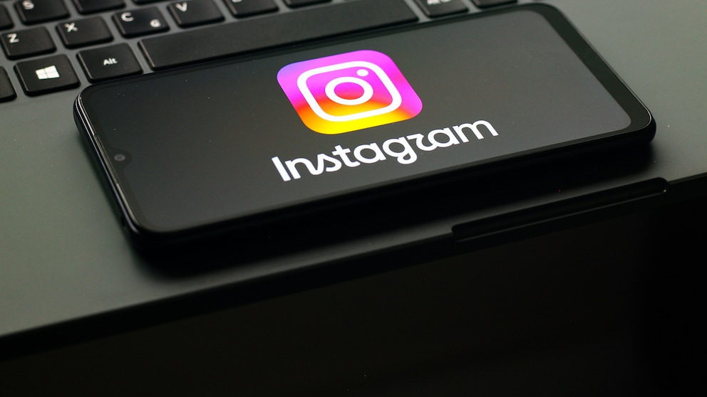 Auf einem Smartphone ist das Instagram-Logo zu sehen, das Gerät liegt auf der Tastatur eines Laptops