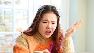 Eine Person sitzt vor einem Laptop und hebt eine Hand mit geöffneter Handfläche neben das frustrierte Gesicht