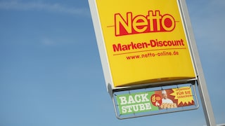 Gelbes Netto-Markenschild mit roter Aufschrift vor blauem Himmel, darunter ein Werbebanner für die Backstube