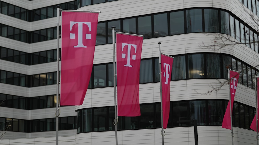 Auf dem Bild stehen mehrere magentafarbene Telekom-Flaggen mit dem weißen „T“-Logo vor einem modernen Bürogebäude. Weitere Flaggen sind am rechten Bildrand zu sehen, im Hintergrund erstreckt sich die helle Fassade mit großen dunklen Fensterflächen.