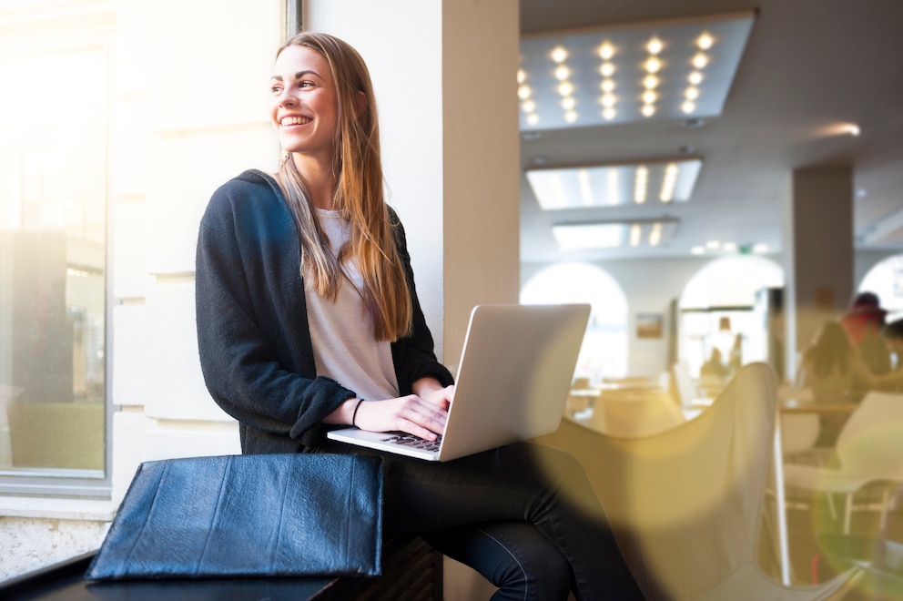 Digital Nomad: Frau lacht und schaut aus Fenster mit LapTop