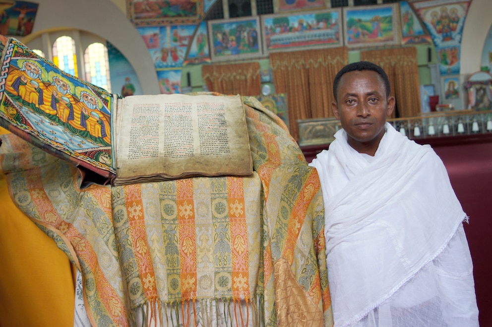 Diakon Zemikael Brhane in der neuen Kirche der Heiligen Maria von Zion in Axum neben einem alten religiösen Buch