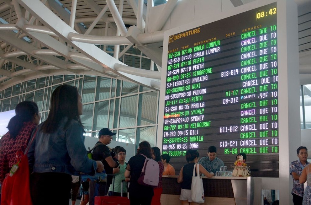 Reisende übrpüfen Flugverspätungen am Ngurah Rai Flughafen in Denpasar auf Bali