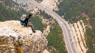 Ein Mann sitzt auf einem Felsen und Blick tief herab