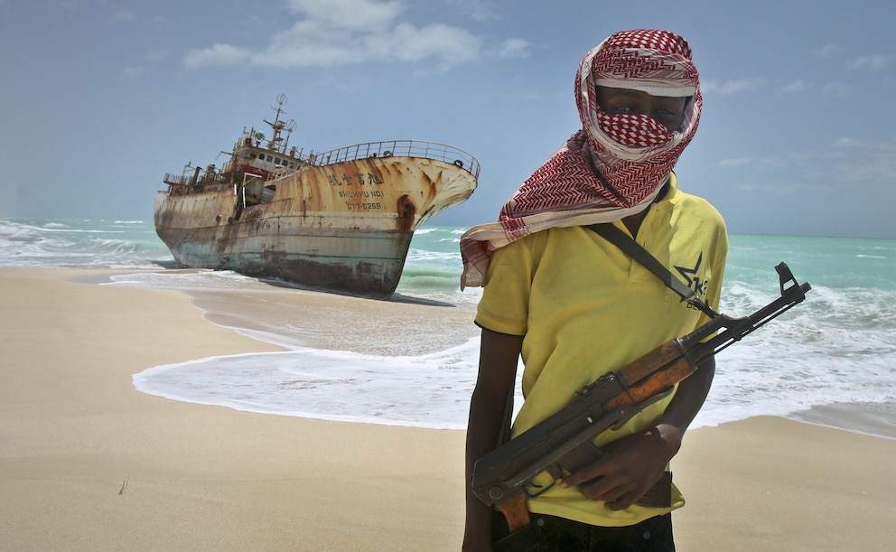 Ein Pirat mit Kalaschnikow am Strand von Hobyo vor einem Schiffswrack