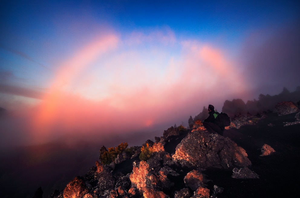 Ein Nebelbogen über der kanarischen Insel La Palma wird von der Abendsonne in rotes Licht getaucht