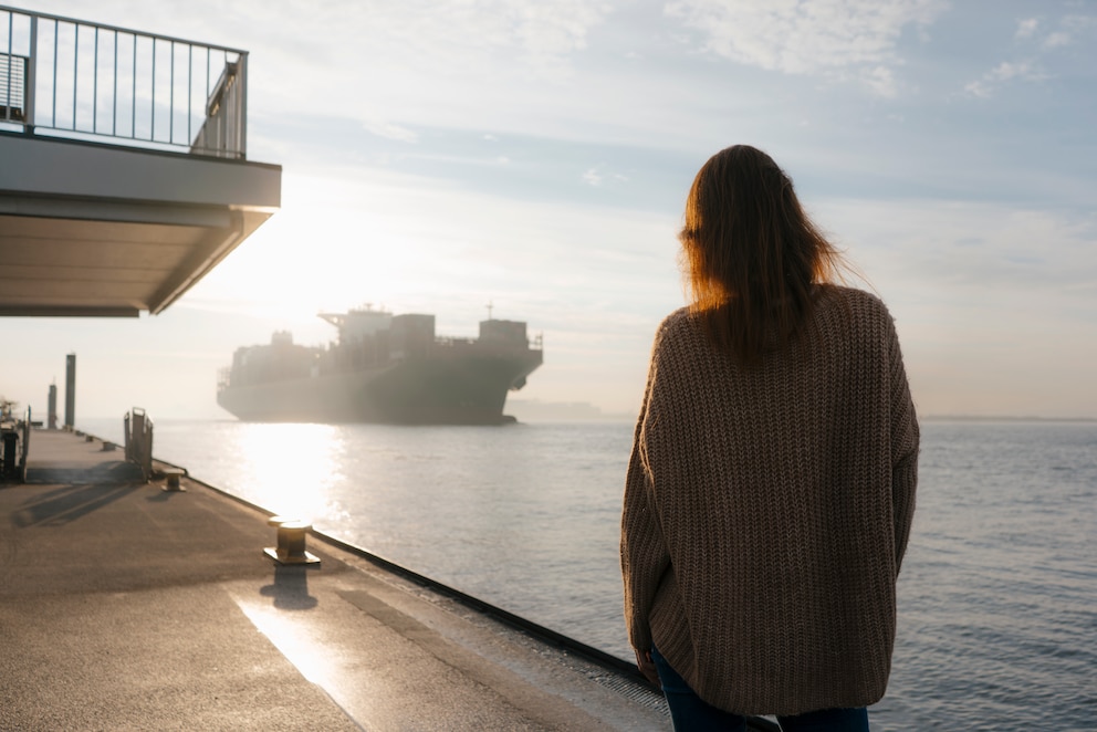 Frau wartet am Hafen auf ein Frachtschiff