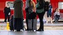 Reisende warten am Bahnsteig auf ihren Zug