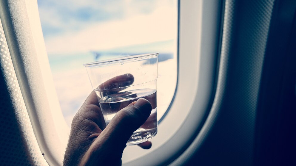 Mann trinkt Wasser im Flugzeug