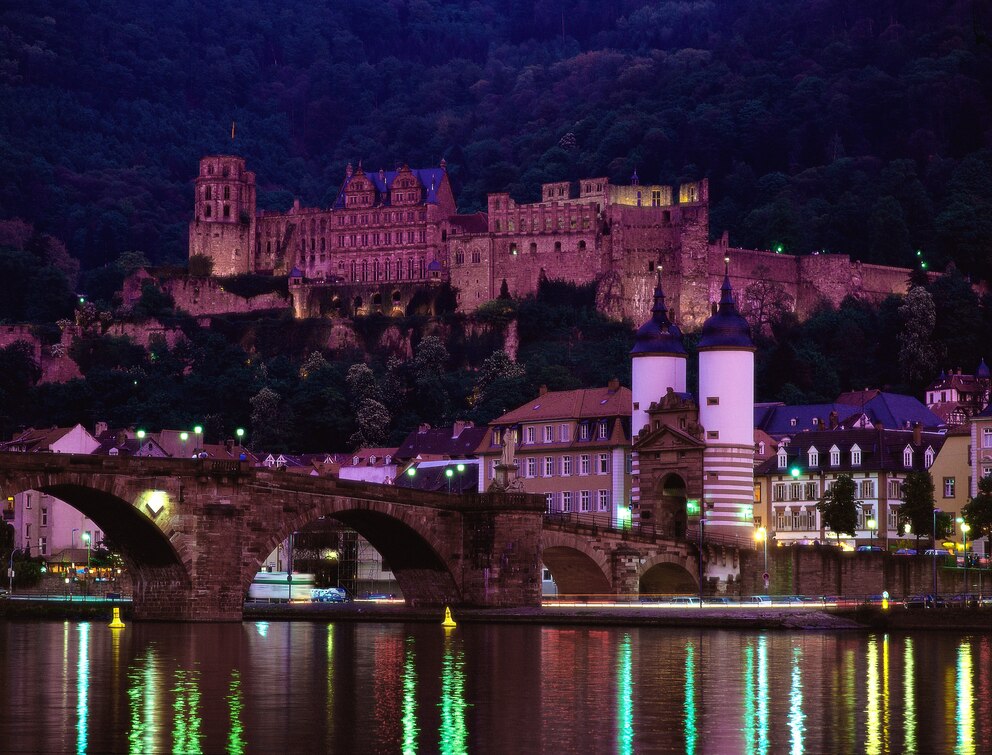 Über dem Fluss Neckar und der Stadt erstrahlt in nächtlicher Beleuchtung das Schloss Heidelberg