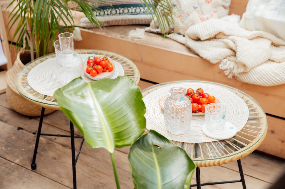 Rattanmöbel und Quasten-Kissen schaffen beim Urlaub zuhause auf dem Balkon oder der Terrasse eine gemütliche Atmosphäre.