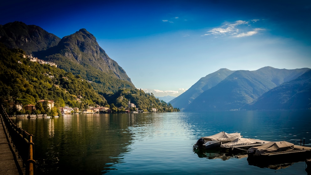 Blick über den Luganersee: Strahlende Fassaden mit Fischerboot im Vordergrund