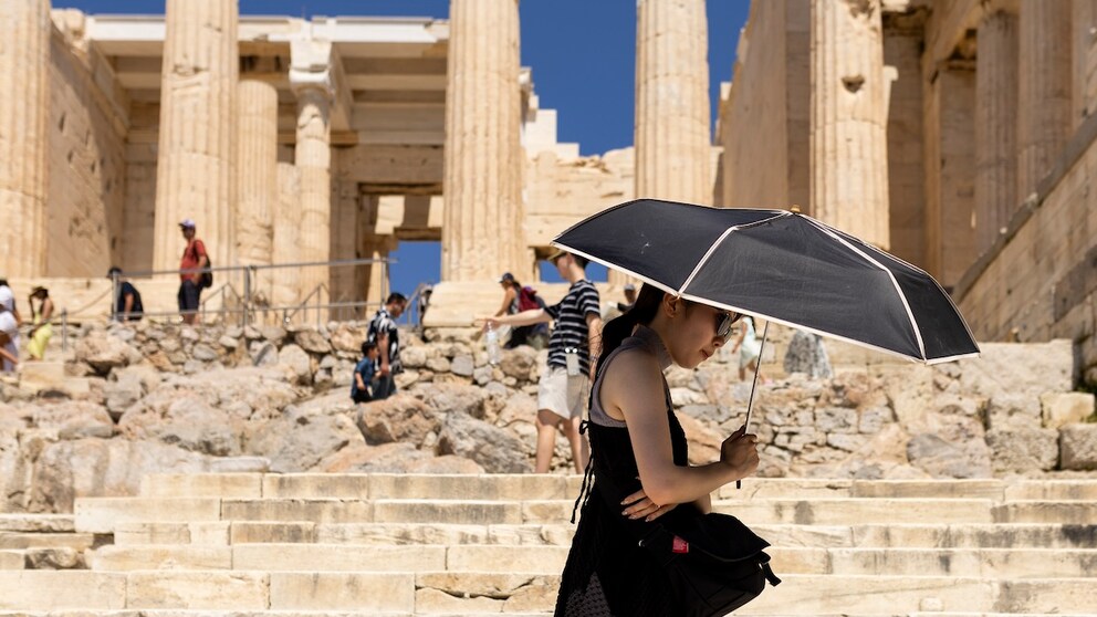 Eine Touristin sucht Schatten unter einem Schirm während ihres Besuchs auf der Akropolis. Griechenland ist in diesem Jahr besonders früh von großer Hitze in Europa betroffen.