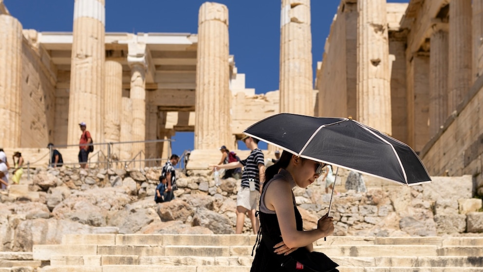 Eine Touristin sucht Schatten unter einem Schirm während ihres Besuchs auf der Akropolis. Griechenland ist in diesem Jahr besonders früh von großer Hitze in Europa betroffen.