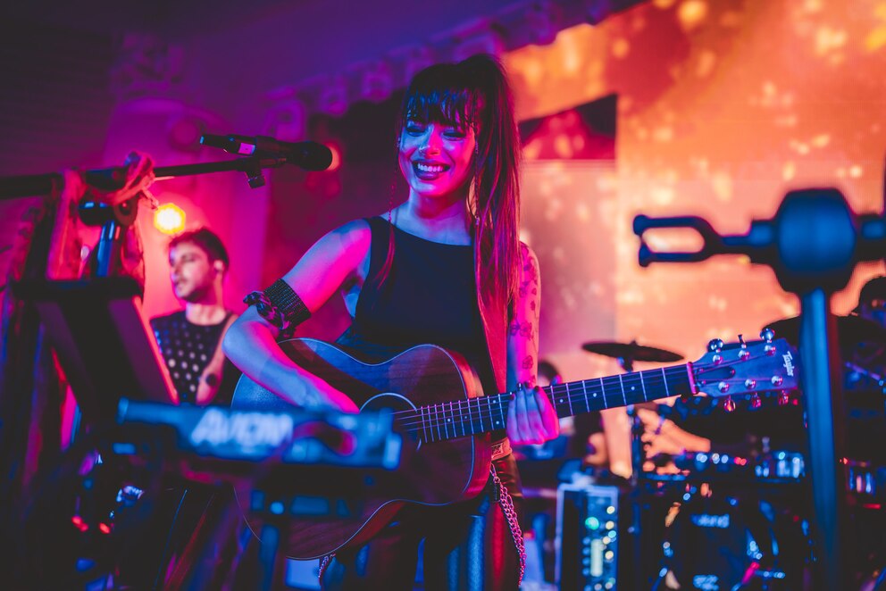 Eine Band spielt auf einer Bühne, die Frontsängerin spielt nebenbei Gitarre.