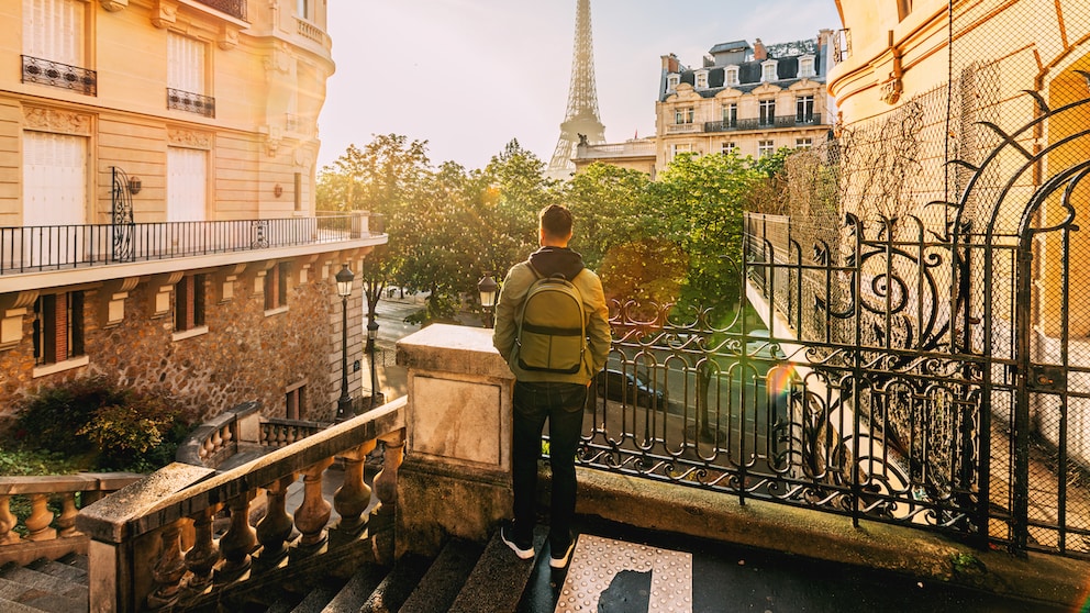 Reisender mit Rucksack vor dem Eiffelturm: Unsere Autorin nennt fünf Dinge, die sie vor ihrem Frankreich-Urlaub gerne gewusst hätte