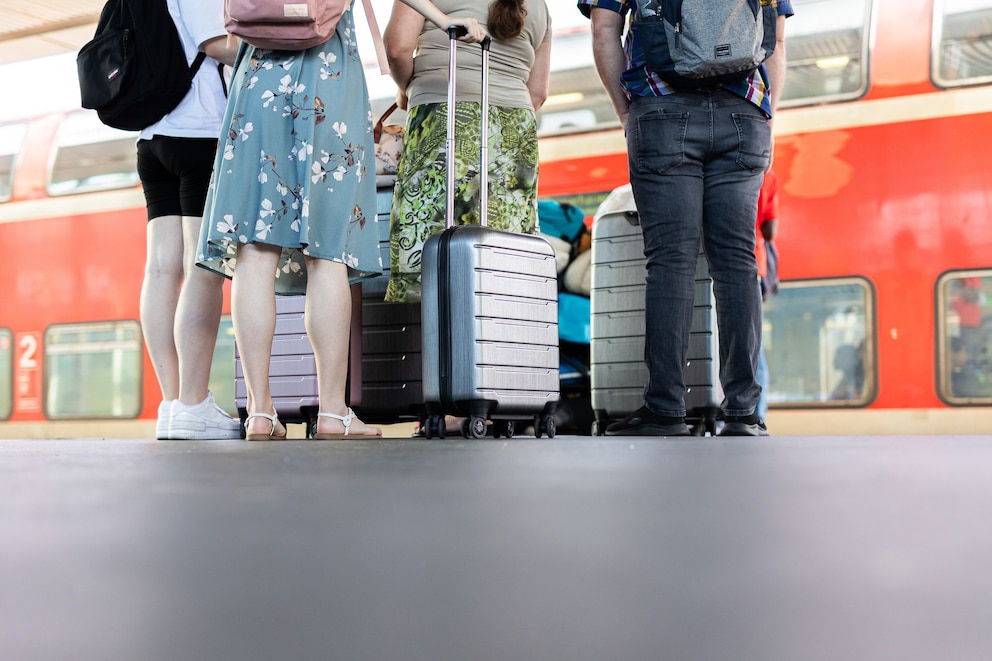 Personen stehen mit Koffern auf einem Bahnsteig