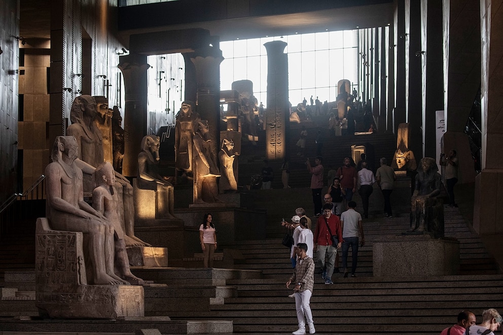 Auf der großen Treppe im Eingangsbereich laufen Besucher an altägyptischen Statuen vorbei