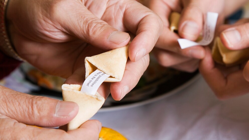 Hände öffnen einen Glückskeks: Er gehört für viele zum Besuch in einem chinesischen Restaurant – dabei liegt der Ursprung des Gebäcks eigentlich woanders