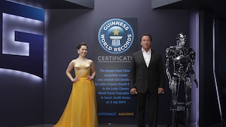 Emilia Clarke und Arnold Schwarzenegger posieren während der Seouler Premiere von „Terminator Genisys“ vor dem Schild, das auf einen Eintrag im Guinness-Buch der Rekorde für die größte Kinoleinwand der Welt hinweist