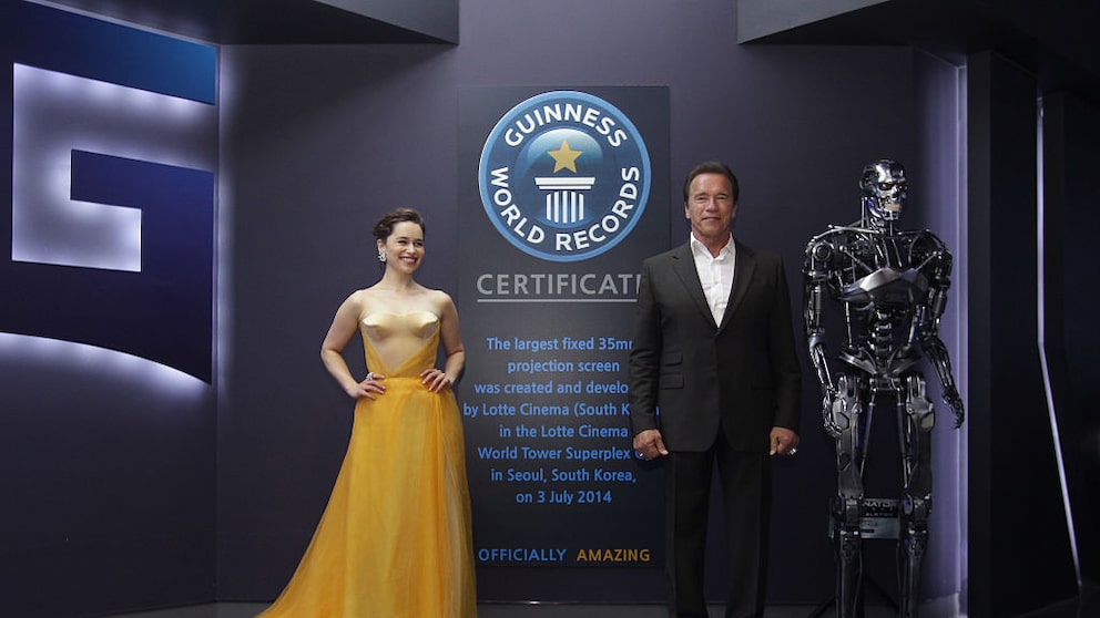 Emilia Clarke und Arnold Schwarzenegger posieren während der Seouler Premiere von „Terminator Genisys“ vor dem Schild, das auf einen Eintrag im Guinness-Buch der Rekorde für die größte Kinoleinwand der Welt hinweist