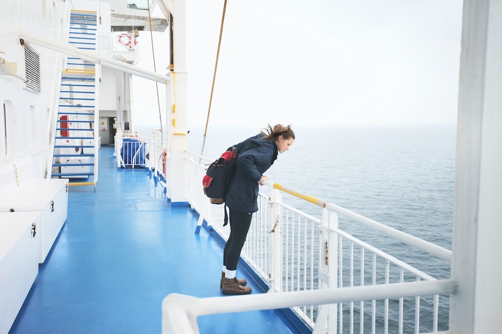Frau guckt über Reling auf Kreuzfahrtschiff