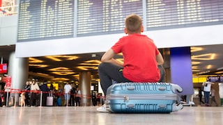 Junge sitzt auf Koffer am Flughafen und wartet